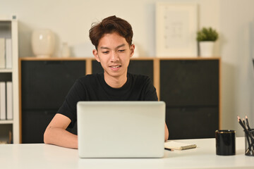 Young asian man freelancer in casual clothes sitting in home office and typing report on a laptop computer