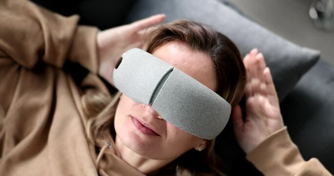 Tired woman puts massage glasses on eyes lying on couch