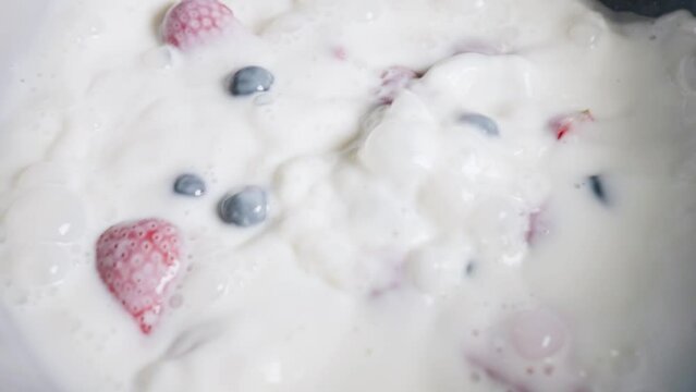Fresh strawberries and blueberries fall into milk in slow motion