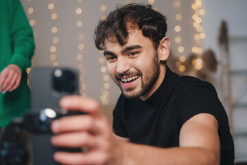 Portrait of positive young man filming tutorial video trend for social network, using cellphone on tripod in living room. Internet technology, digital marketing