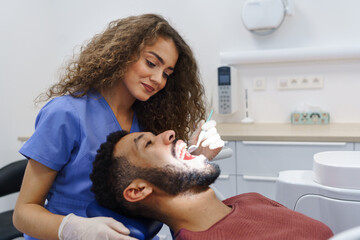 Young woman dentist doing preventive examination to multiracial man.
