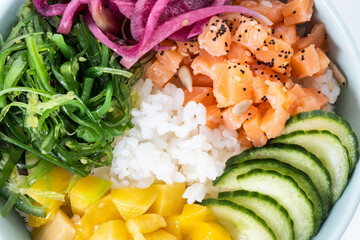 Poke bowl with rice, salmon,cucumber,mango,onion,wakame salad, poppy seeds ands sunflowers seeds isolated on white background