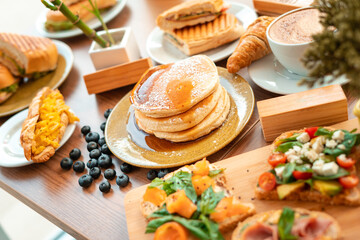 Fototapeta na wymiar Delicious breakfast buffet with pancakes, egg croissants and coffee in wooden table with plants and decoration