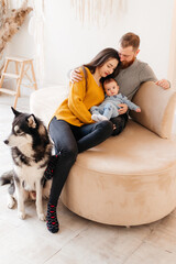 Family with baby boy sitting on the bed with cute dog. Mother and father with their son and doggy together smiling. Beautiful parenthood time. Pet with owners