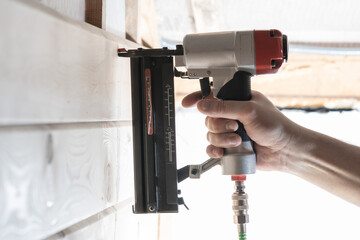 Unrecognizable builder worker hand using pneumatic stapler for wooden board. Framework making,...