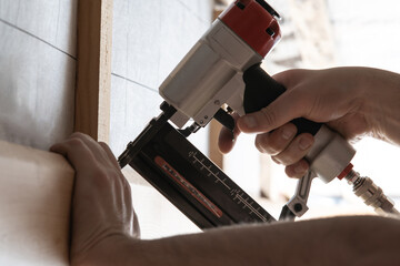 Closeup unrecognizable male hands use pneumatic nailer, stapler gun for wooden plank outdoor. Build...