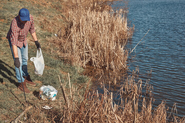 Fototapeta Volunteer and environmental activist cleaning dirty lake shore filled with trash. obraz