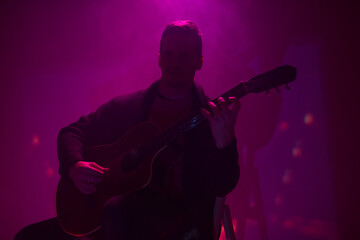 Obraz na płótnie Canvas Musician playing acoustic guitar in a foggy club with colorful lights.