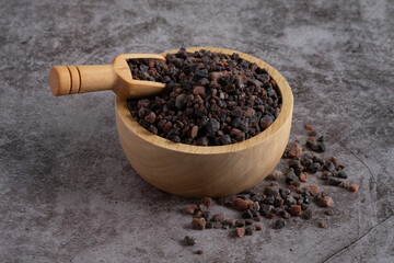 Himalayan black salt, Indian black salt or Kala namak in wooden bowl with wooden scoop on black stone table. Used in cooking, especially in Asian and Indian cuisine. Bath salt spa.