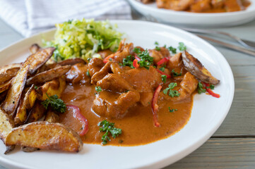Chicken with paprika cream sauce, potato wedges and salad on a plate. Closeup