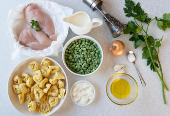 Chicken alfredo ingredients for making or cooking with raw and uncooked chicken breast, green peas, pasta, olive oil, parmesan cheese, cream, onion, garlic and parsley on white background. 
