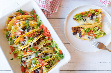 Taco casserole with ground beef, kidney beans, cheese, tomtoes and lettuce in a casserole dish on...