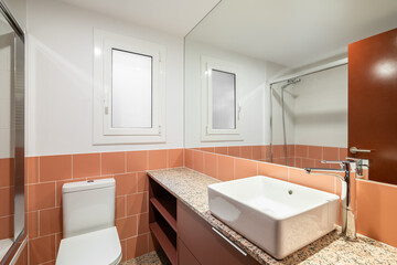Bathroom with a large mirror and terracotta tiles with a countertop, sink and toilet bowl and...