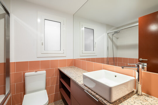 Bathroom with a large mirror and terracotta tiles with a countertop, sink and toilet bowl and window in a renovated apartment. Concept of renovation in an old apartment