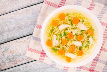 Homemade chicken soup with noodles and vegetables in a white bowl, on a wooden background.