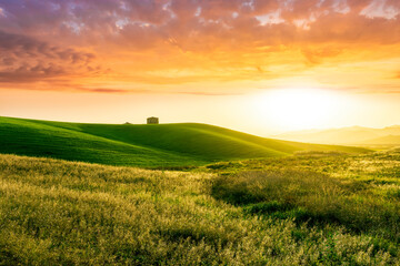 countryside sunset in green hills of spring fields with old castle farm and mountains on background of evening landscape