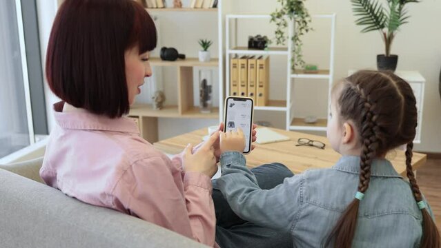 Mother and daughter holding cell phone with fashion webstore site on screen. Excited family woman and her smart kid finding big discount on clothes while shopping at home.