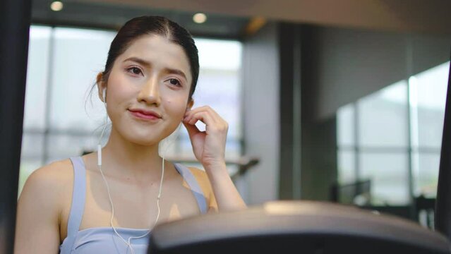 Young asian athletic woman with perfect shape body wearing earphones is choosing workout music with smart phone to listen while practicing in gym, Technology to stay fit and motivated 