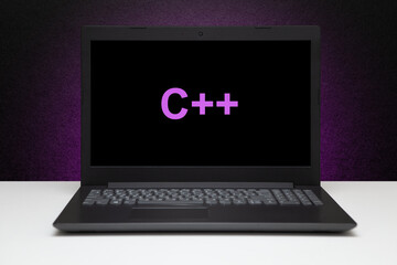C plus text on laptop screen on textured black background with purple light. Learn C plus...