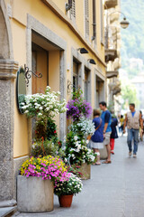 Flowers blossoming in flower pots on old cobblestone street with souvenir shops, restaurants and cafes in Como town, Lake Como, Italy, Europe