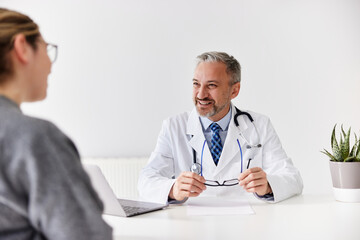 A smiling male doctor sitting with his female patient at his office.