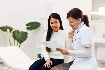 An adult Asian female patient talking with a female doctor about her blood results.