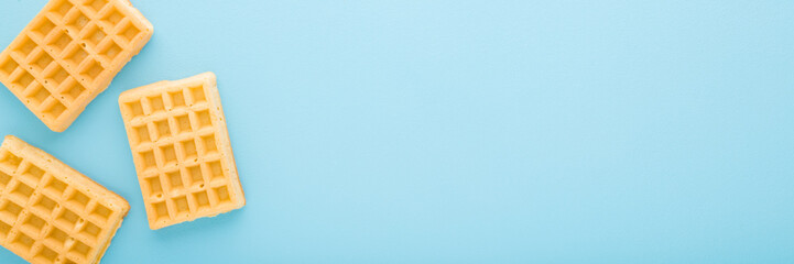 Fresh golden waffles on light blue table background. Pastel color. Wide banner. Closeup. Sweet snacks. Empty place for text. Top down view.