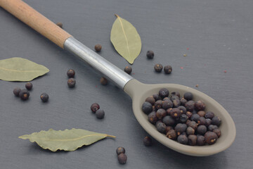 juniper berries in large spoon on dark kitchen slate with laurel leaves