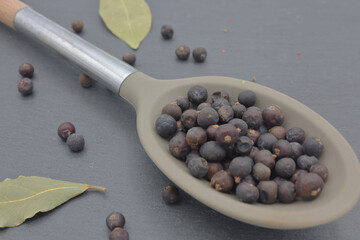 juniper berries in large spoon on dark kitchen slate with laurel leaves