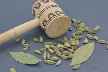 cardamom seeds next to wooden cooking mallet over dark slate