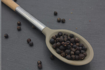 juniper berries in large spoon on dark kitchen slate 