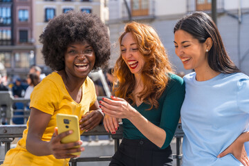 Three multiracial young women taking a selfie in the city, outdoors, friendship, feminist and technology concept