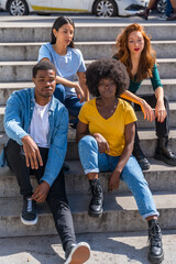 Fototapeta premium Portrait of happy multiethnic friends sitting on stairs in the city, young models