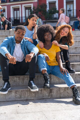 Portrait of happy multiethnic friends sitting on stairs in the city, young models