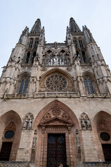 Fototapeta na wymiar Entrada principal de la Catedral de Burgos con las vitrinas y las columnas en lo alto bajo un cielo nublado en un día frío de primavera.