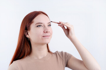 Joyful redhead young woman using makeup brush making up isolated on white background
