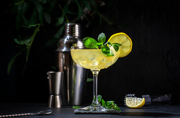 White lady alcoholic cocktail with dry gin, liquor, lemon juice and ice in wine glass. Black background, bar tools