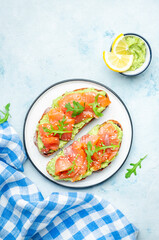 Avocado and salmon sandwich on rye bread with guacamole sauce, arugula and sesame seeds on plate, blue table background, top view