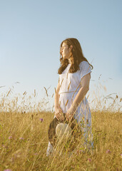 A young girl in glasses, a white summer dress with a straw hat in a field with flowers in the rays of the sunset.