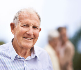 Getting older...but also happier. Portrait of a senior man standing outside with people blurred in the background.