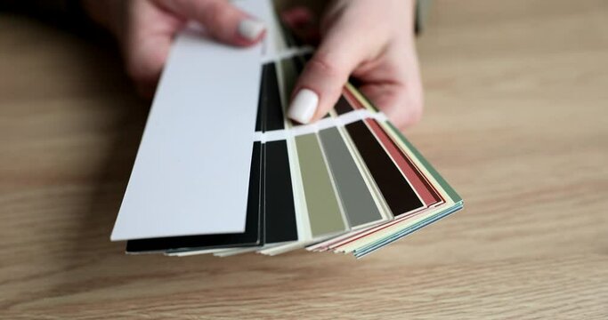 Woman hand holds color samples in palette above table