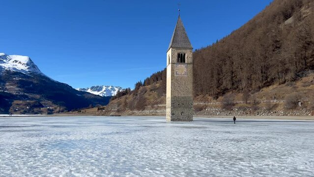 Tilt up shot of the Tower of Graun on a frozen lake on a sunny day.
