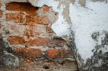 Old cement wall cracked to reveal red bricks inside, poor quality construction.