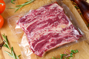 Raw meat in vacuum packaging on a wooden board with spices. Top view