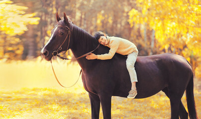 Happy teenager boy child sitting on horse walking in autumn forest