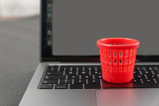 Miniature toy trash can on laptop keyboard. Concept of deleting files and cleaning up information garbage. Cleaning and maintenance of laptop.
