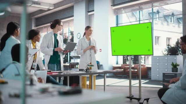 Excited Young Female Specialist Doing a Presentation, Using Green Screen Monitor and Talking to her Colleagues in a Laboratory. Team of Engineers Having a Meeting, Brainstorming While Using Technology