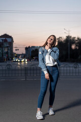 Naklejka premium Pretty young woman walking on city street, summer time. Young stylish girl on evening city background. Vertical frame