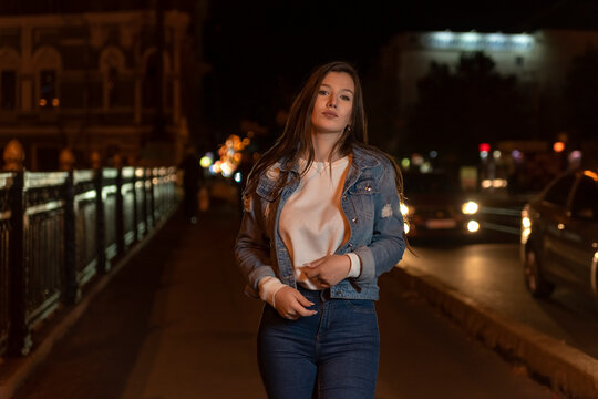 Stylish attractive young woman in denim jacket, evening city background.Portrait of girl student walking on night street