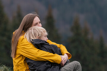 Portrait of young mom and son outside. Mother hugs her child son sitting on halt in woods. Happy family.Hike in the fall
